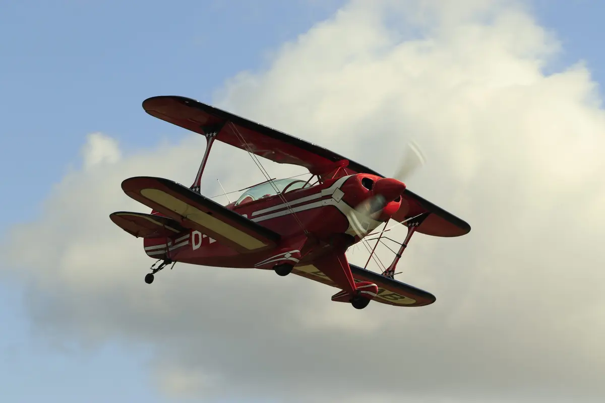 Roter Doppeldecker im Kurvenflug vor Wolken