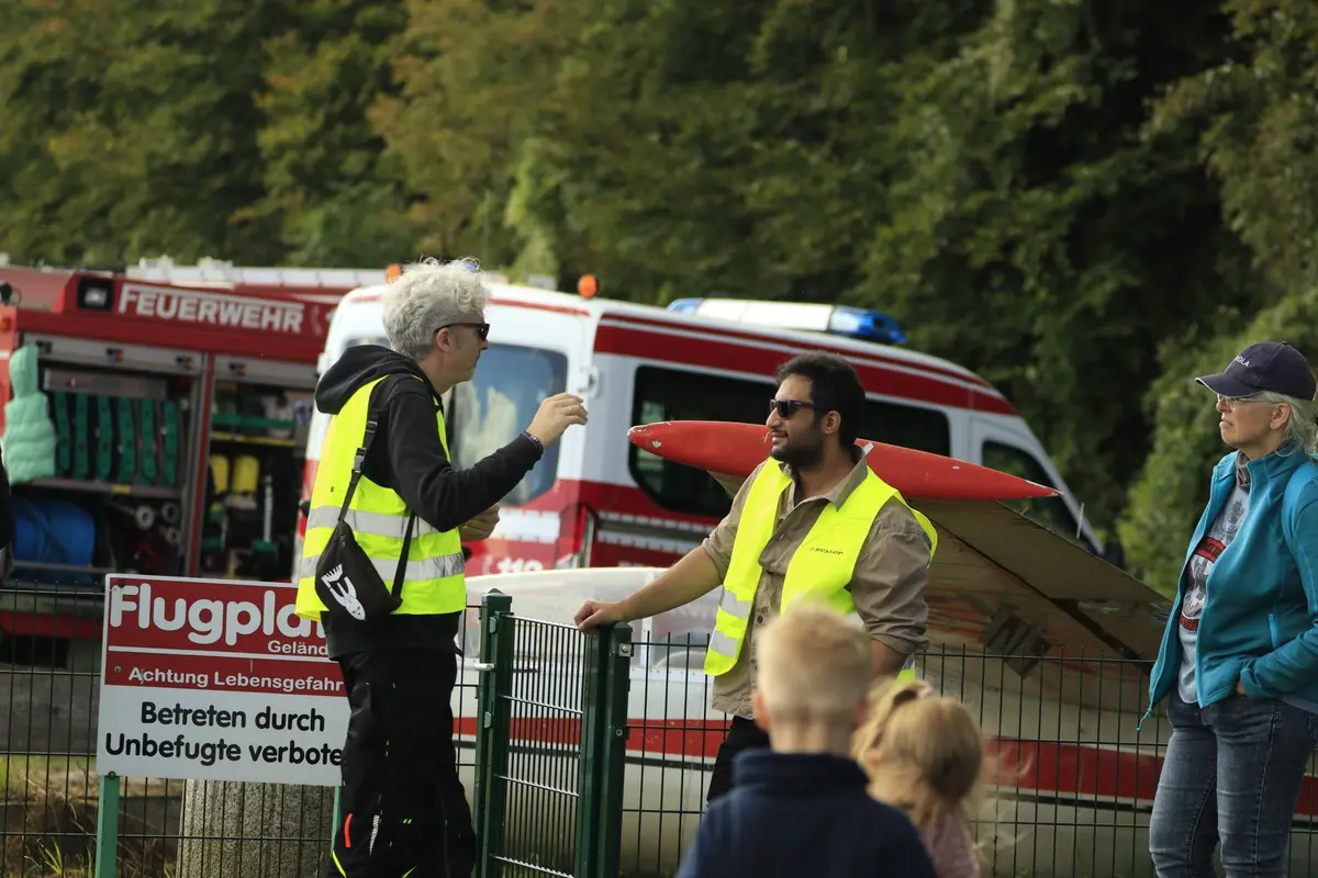 Helfer und Besucher am Zaun vor dem Feuerwehrfahrzeug