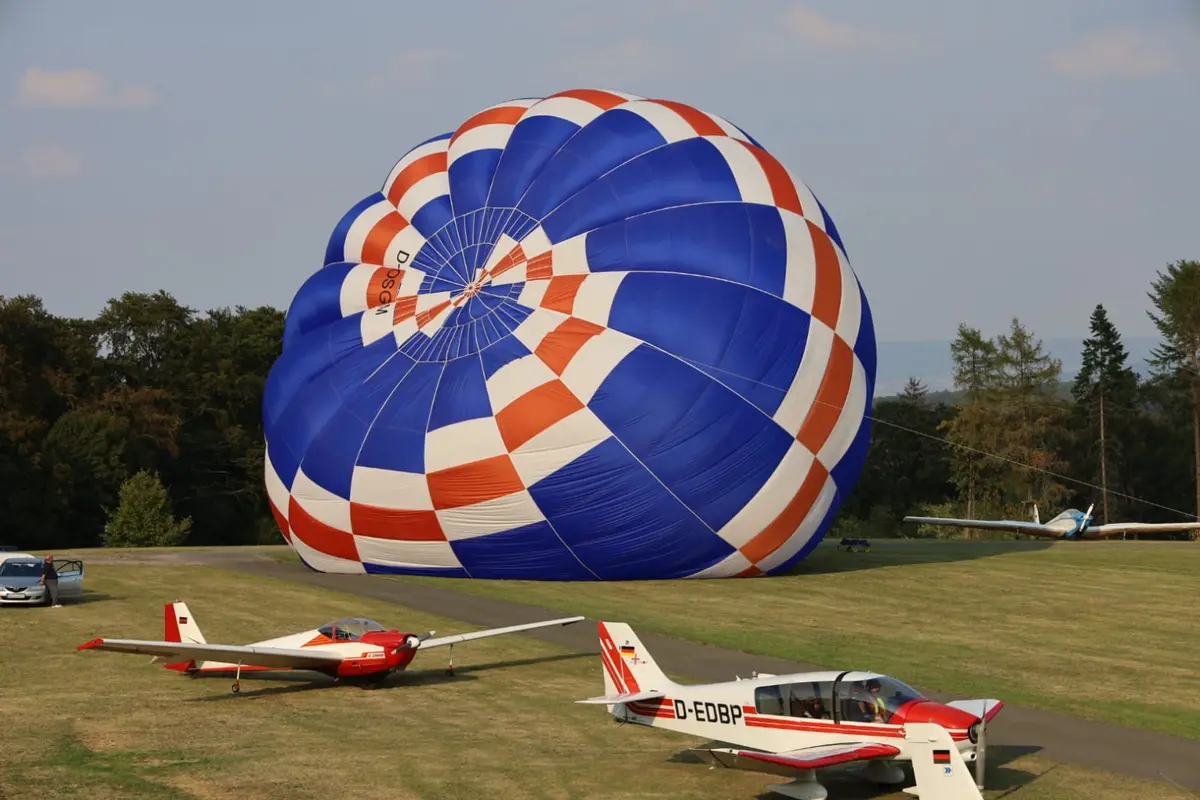 Heißluftballon wird neben abgestellten Robin-Flugzeugen aufgeblasen