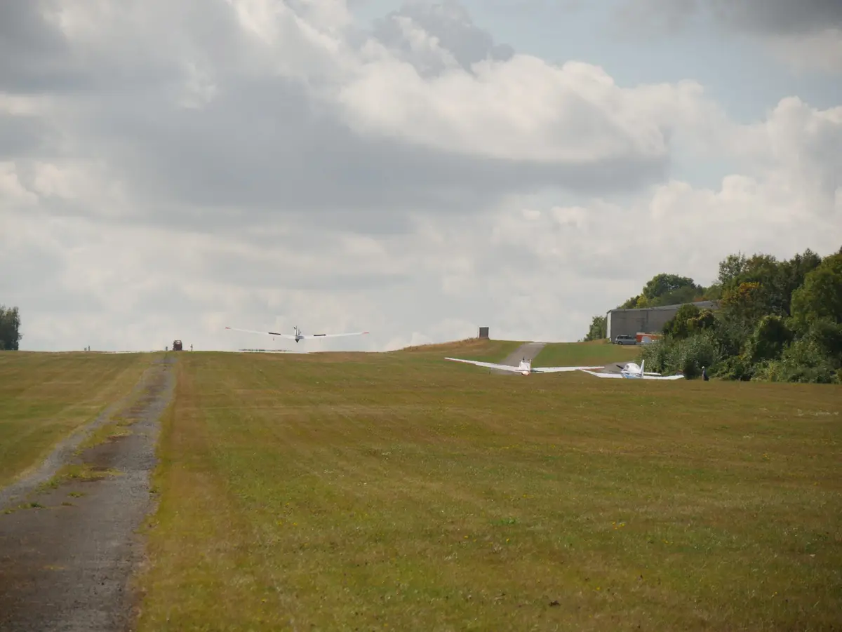 Blick über die Graspiste mit Flugzeugen in der Ferne