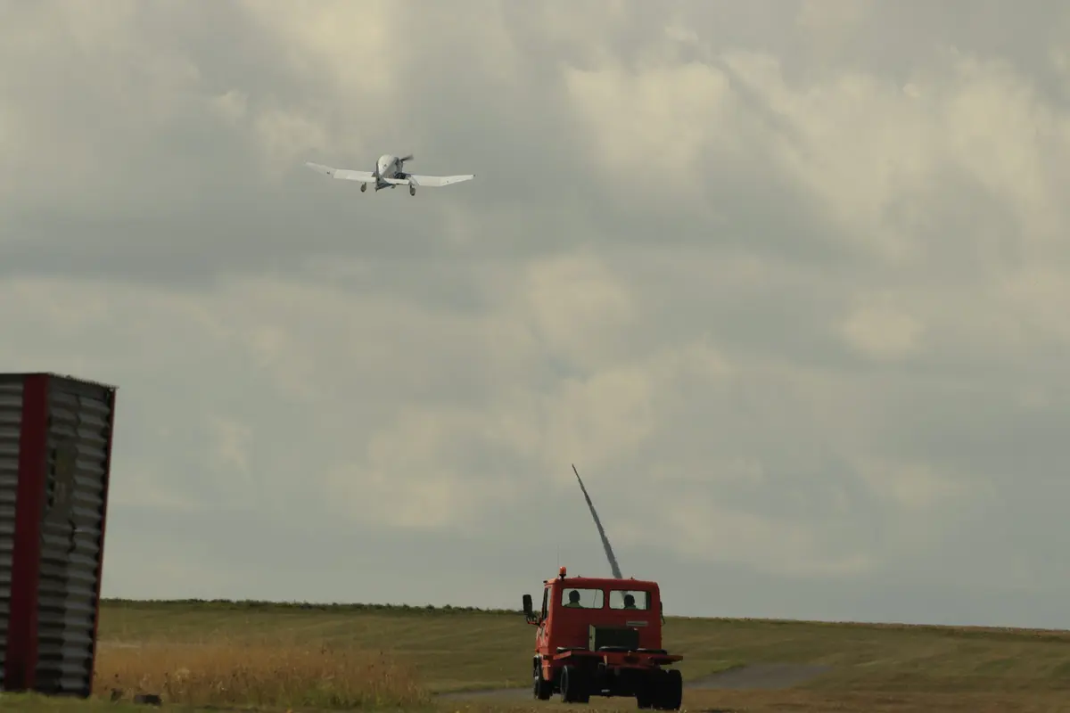 Seilwinde am Pistenende, darüber ein Flugzeug im Anflug